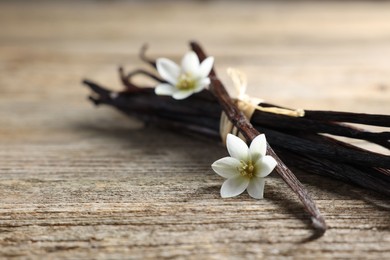 Photo of Bunch of vanilla pods and flowers on wooden table, closeup