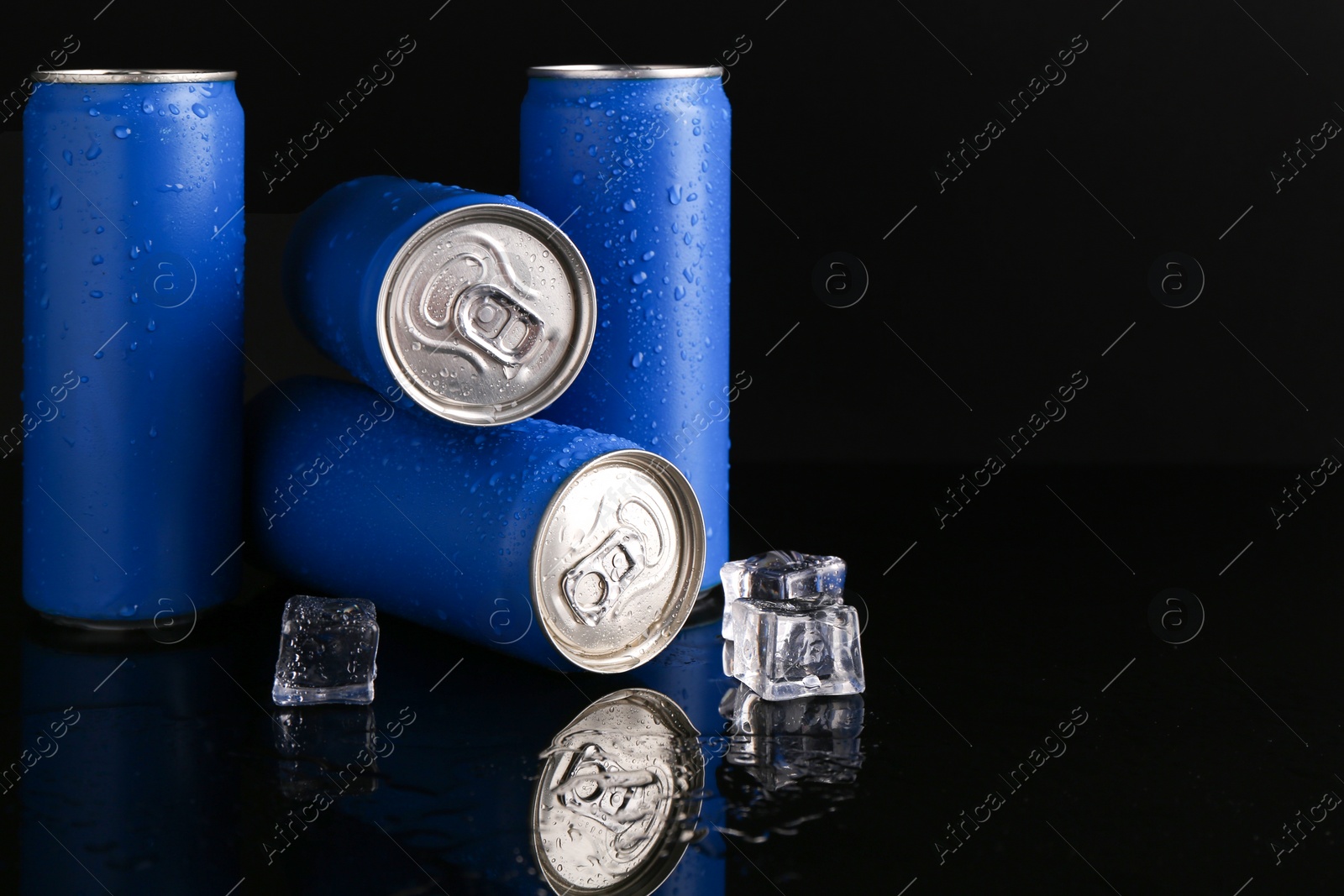 Photo of Energy drinks in wet cans and ice cubes on black background, space for text