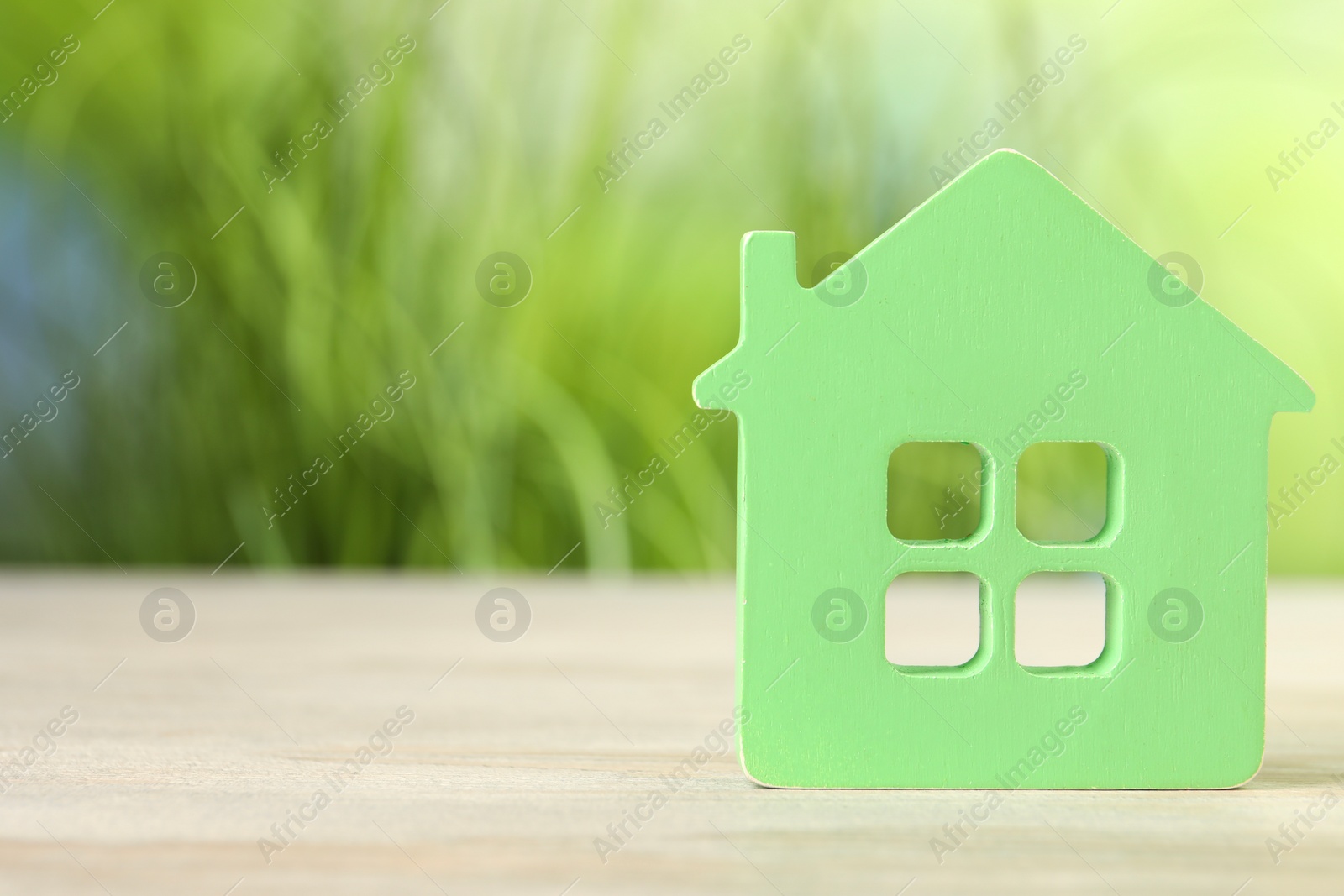 Photo of Mortgage concept. House model on white wooden table against blurred green background, space for text