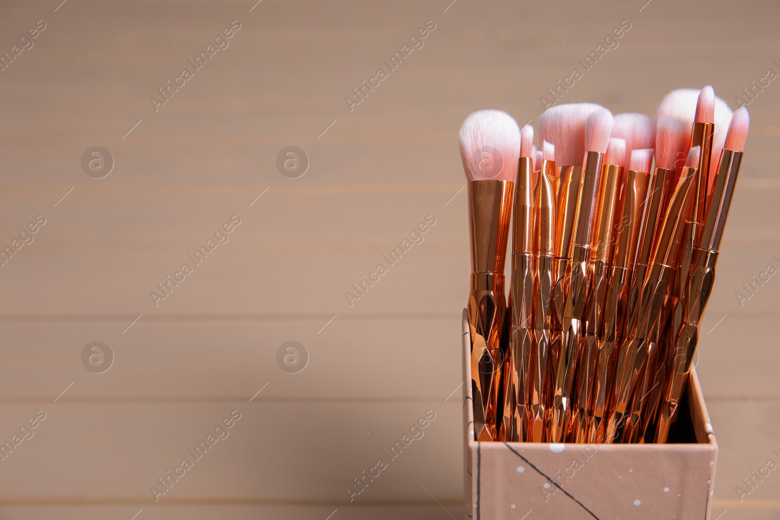 Photo of Organizer with professional makeup brushes on wooden table. Space for text