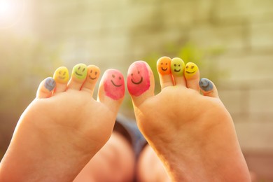 Photo of Teenage girl with smiling faces drawn on toes outdoors, closeup