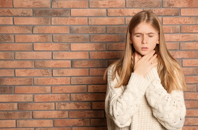 Photo of Teenage girl suffering from cough near brick wall. Space for text