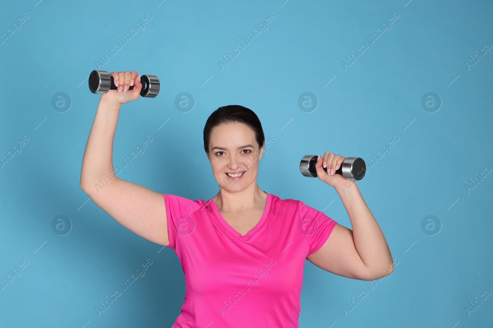 Photo of Happy overweight woman doing exercise with dumbbells on light blue background