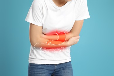Woman suffering from stomach ache on light blue background, closeup. Illustration of unhealthy gastrointestinal tract