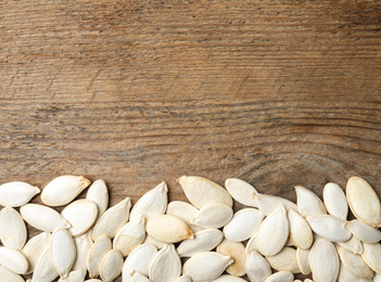 Raw pumpkin seeds and space for text on wooden background, flat lay. Vegetable planting