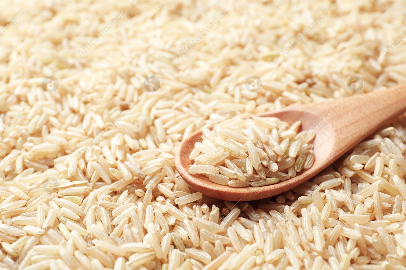 Photo of Wooden spoon with raw brown rice on cereal, closeup view