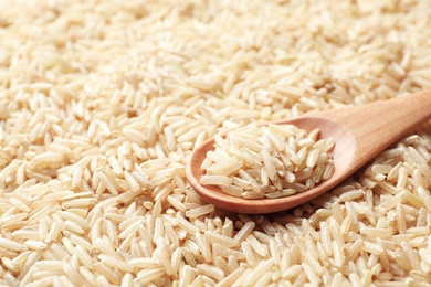 Wooden spoon with raw brown rice on cereal, closeup view