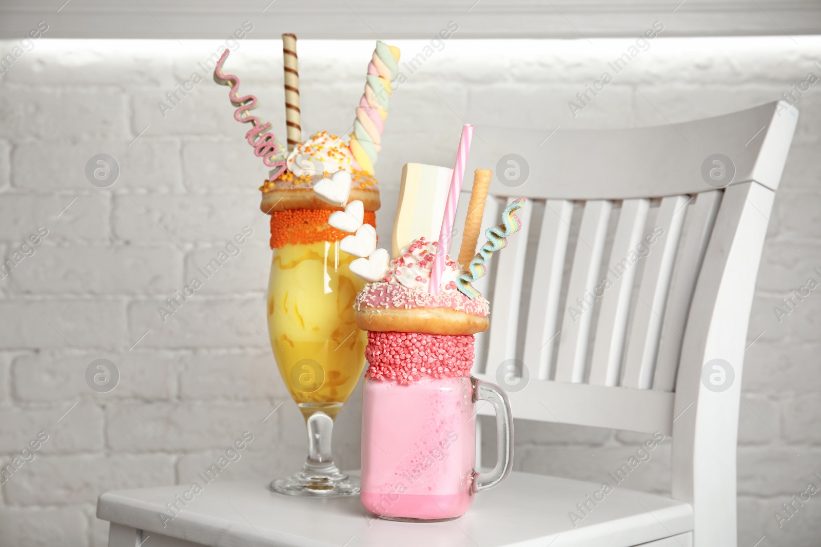 Photo of Tasty milk shakes with sweets in glassware on chair near brick wall