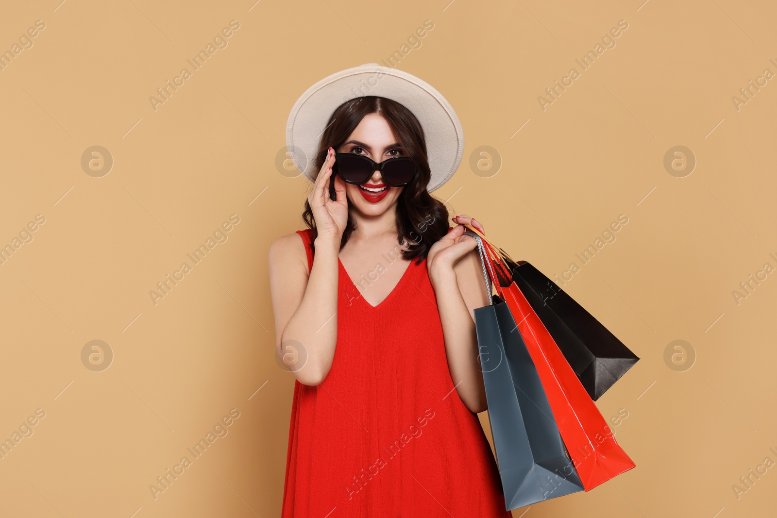 Photo of Beautiful young woman with paper shopping bags on beige background