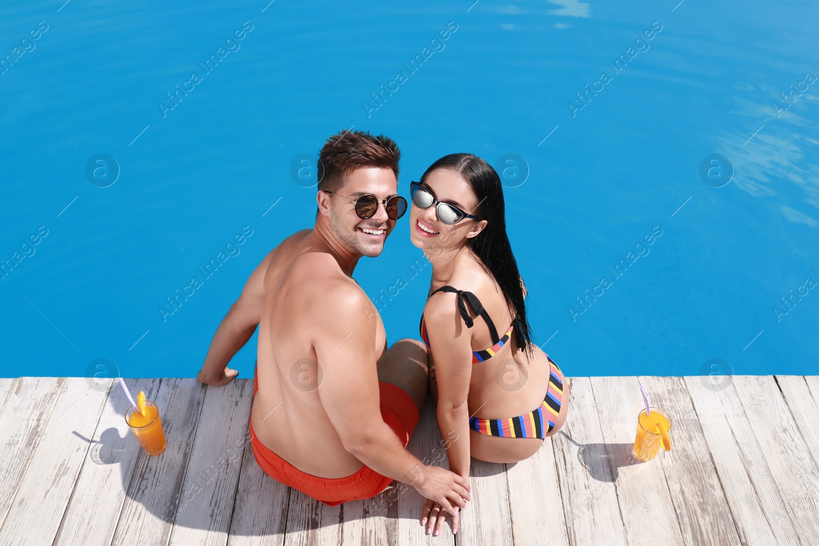 Photo of Woman in bikini with boyfriend near outdoor pool. Happy young couple