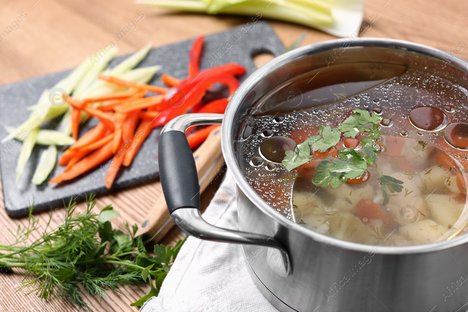 Photo of Pot of delicious vegetable bouillon and ingredients on wooden table, closeup