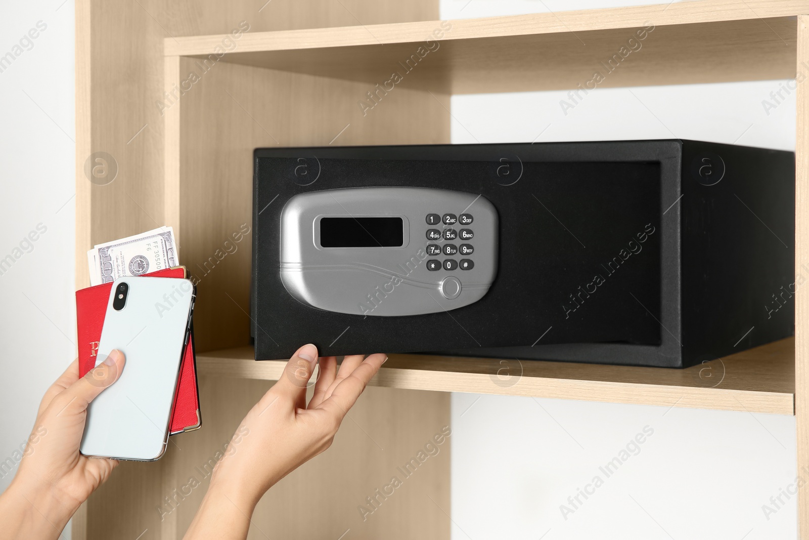 Photo of Woman putting smartphone, passport and money into steel safe, closeup