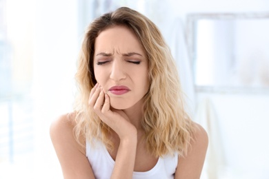 Young woman suffering from toothache indoors