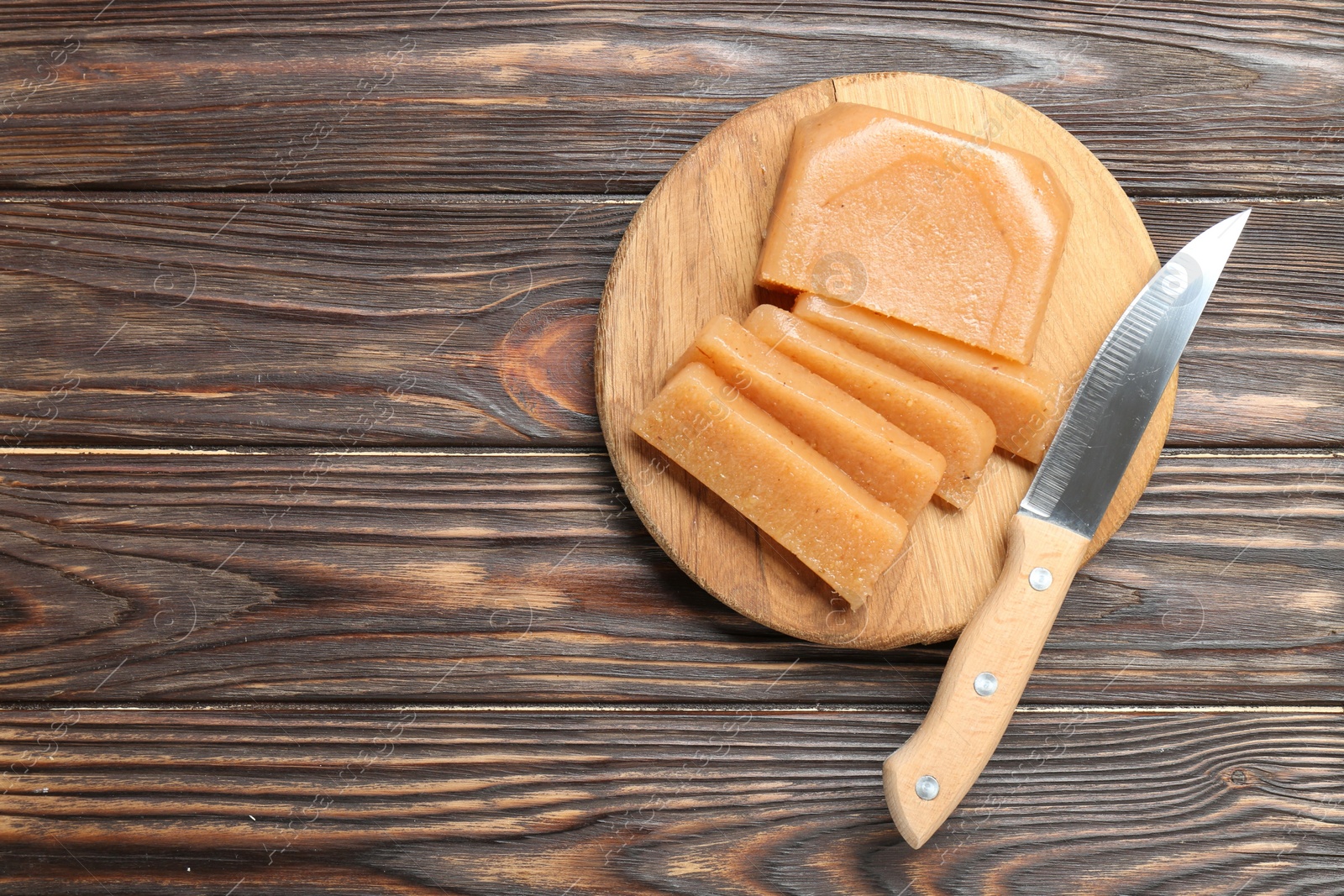 Photo of Tasty sweet quince paste and knife on wooden table, top view. Space for text