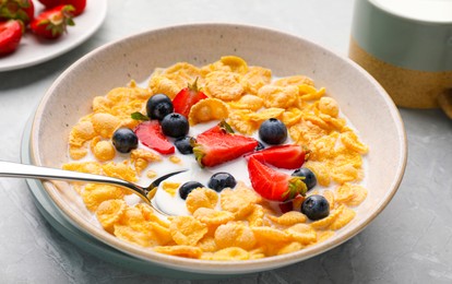 Photo of Bowl of tasty crispy corn flakes with milk and berries on light grey table, closeup