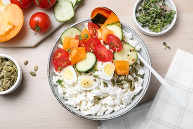 Fresh cottage cheese with seeds, vegetables and eggs in bowl on wooden table, flat lay