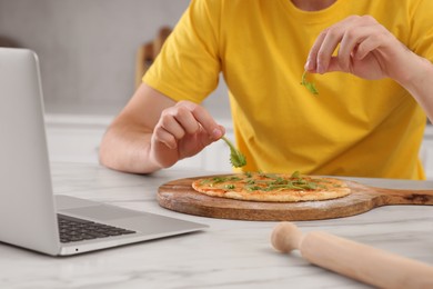 Photo of Man making pizza with cooking online course on laptop in kitchen, closeup. Time for hobby