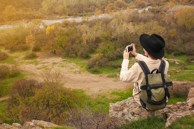 Traveler with backpack taking photos near mountain river, back view. Autumn vacation