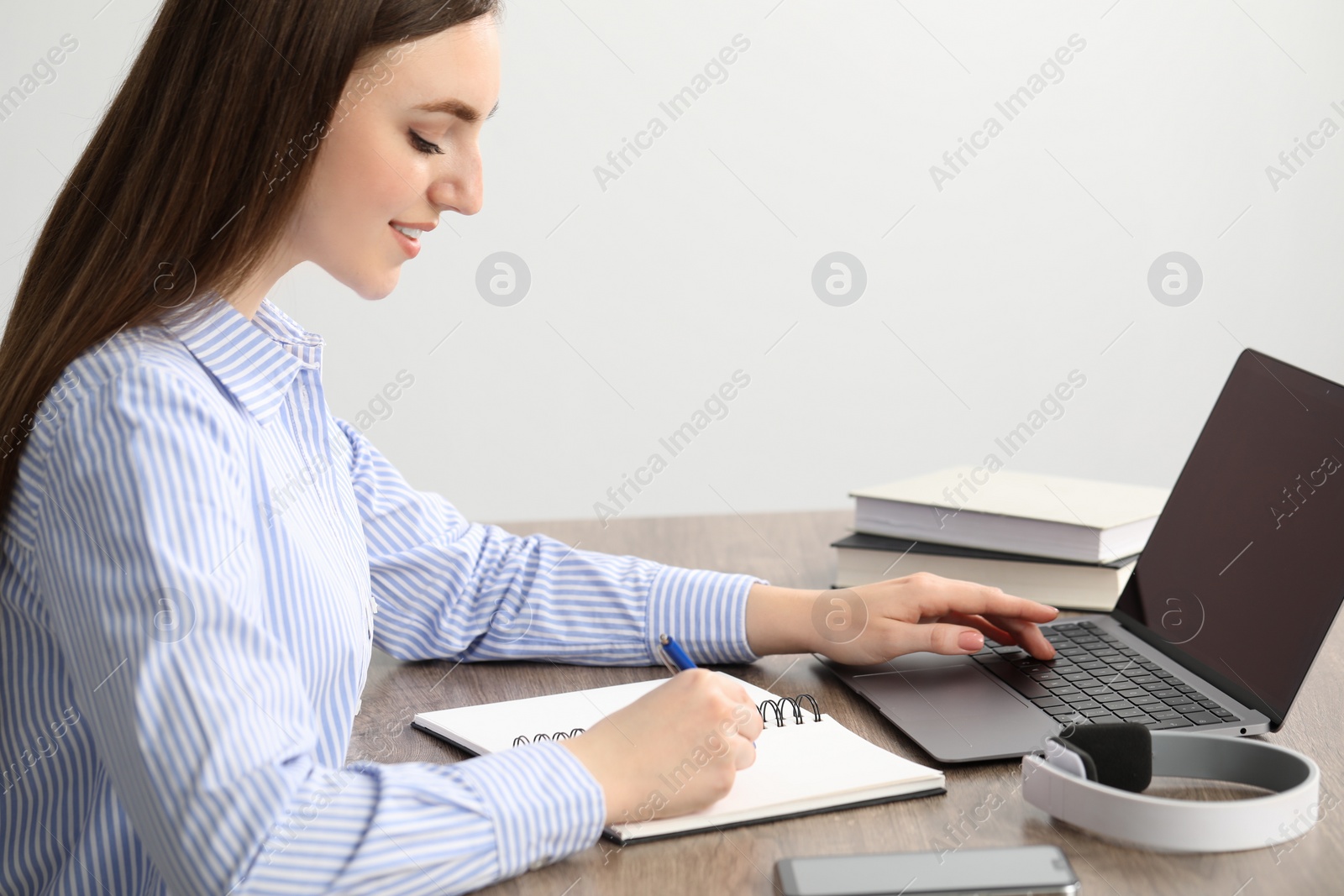 Photo of E-learning. woman taking notes during online lesson at table indoors