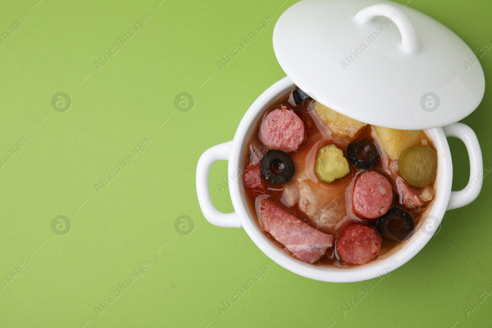 Photo of Meat solyanka soup with thin dry smoked sausages in pot on light green background, top view. Space for text