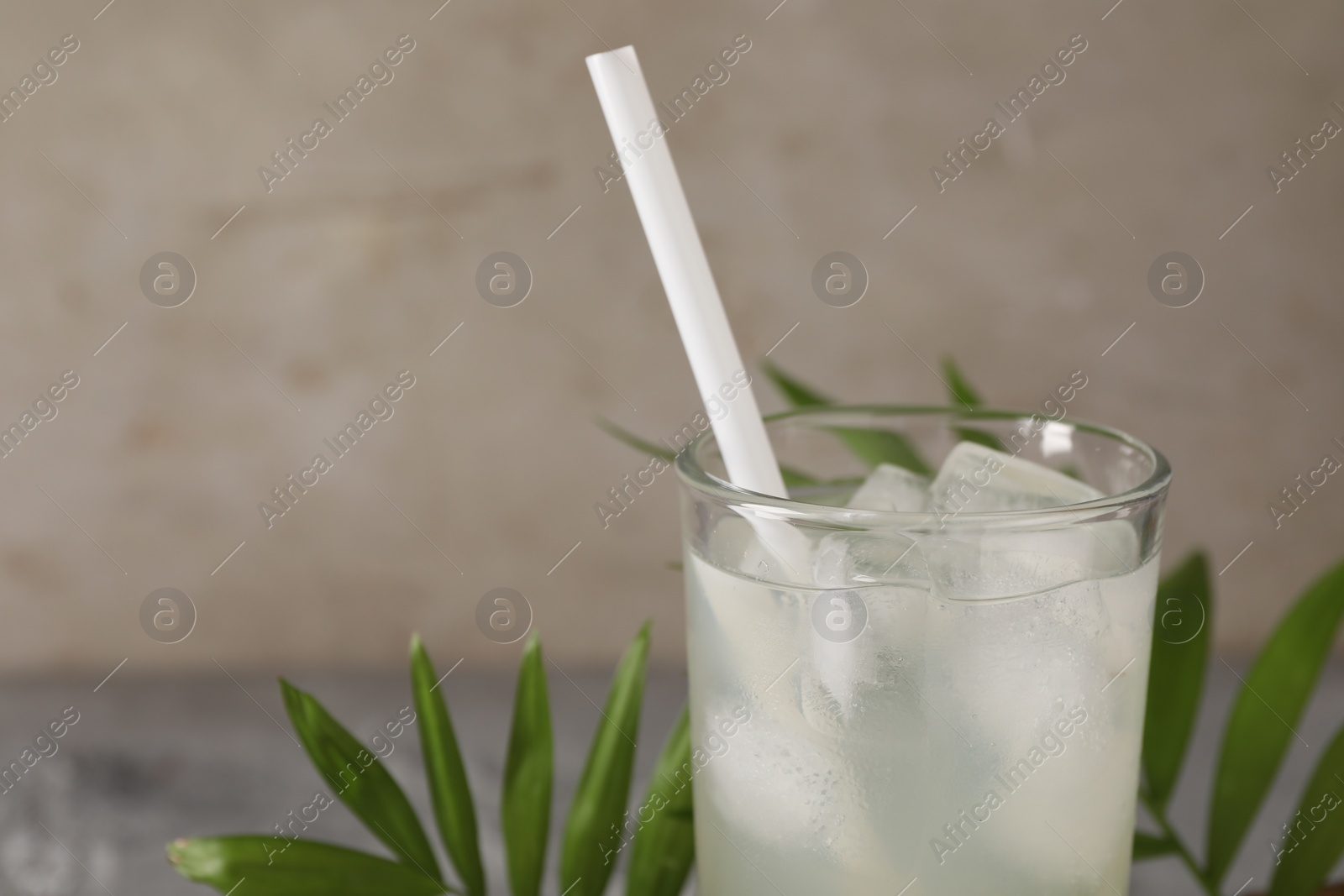 Photo of Glass of coconut water, ice cubes and leaves on grey table, closeup. Space for text