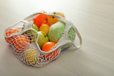 Photo of Net bag with vegetables and fruits on wooden table