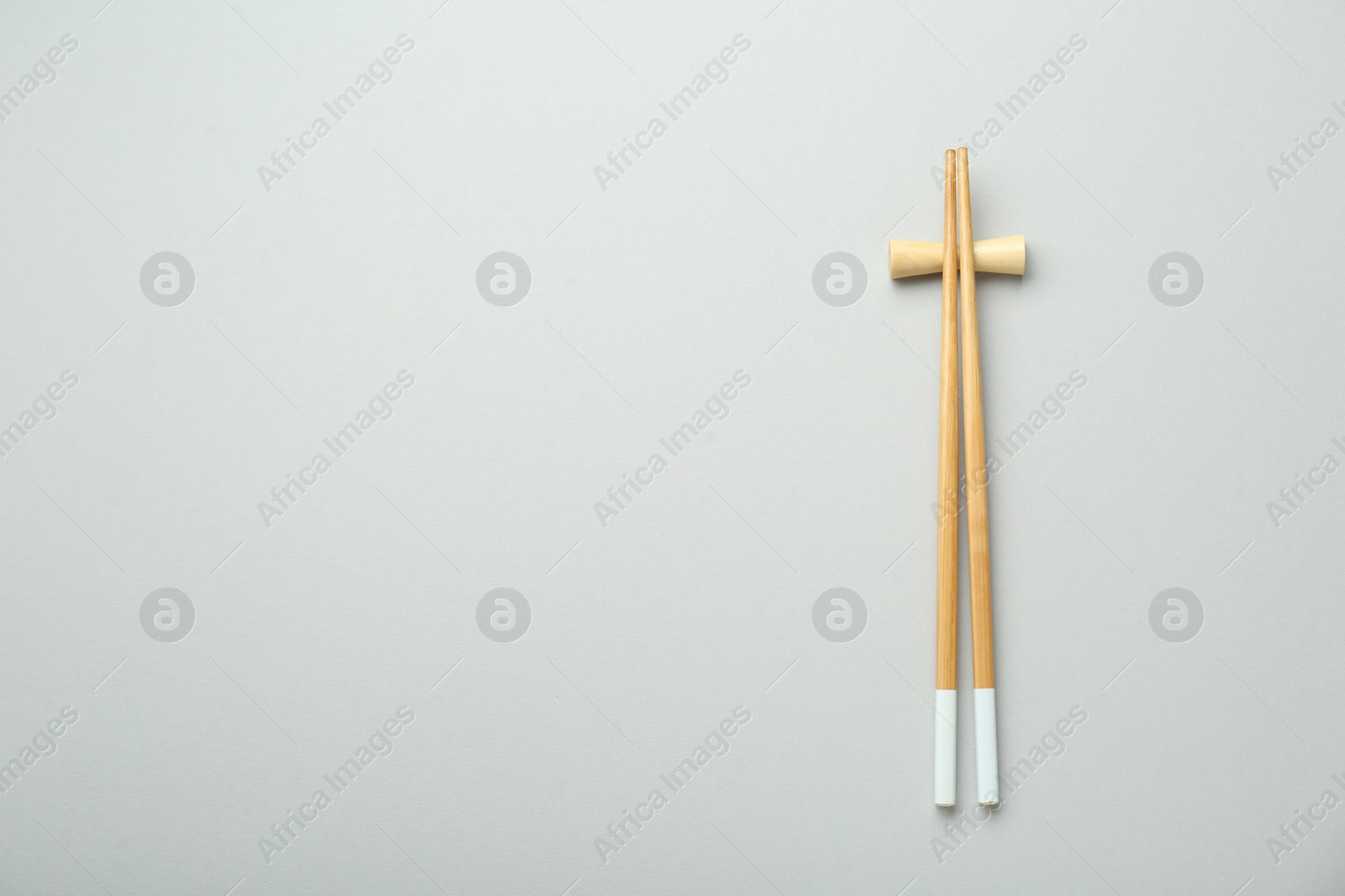 Photo of Pair of wooden chopsticks with rest on light grey background, top view. Space for text