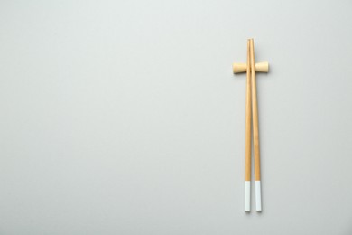Photo of Pair of wooden chopsticks with rest on light grey background, top view. Space for text