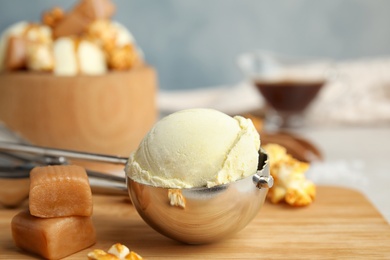 Photo of Delicious ice cream in scoop, caramel and popcorn on wooden board