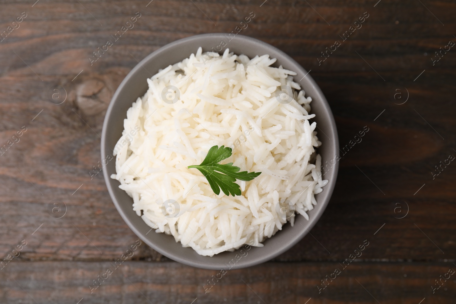 Photo of Bowl of delicious rice with parsley on table, top view