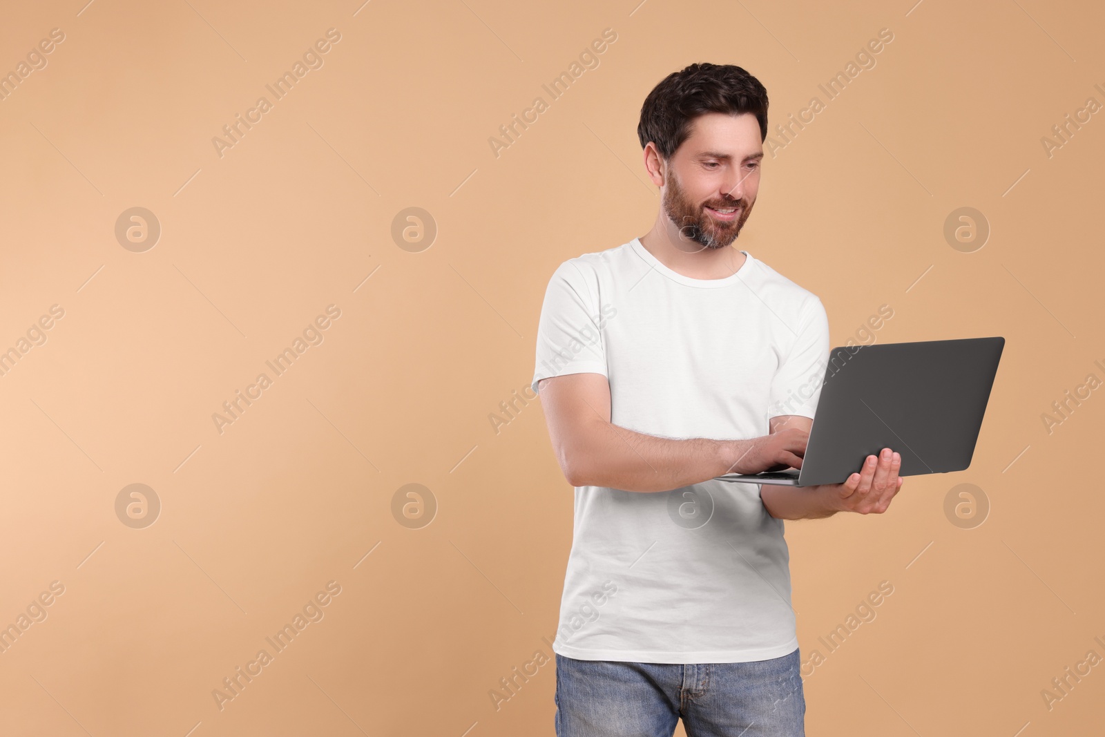 Photo of Happy man with laptop on beige background. Space for text