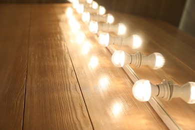 Modern mirror with light bulbs on wooden table, closeup