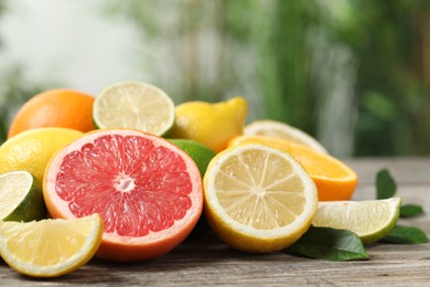 Different fresh citrus fruits and leaves on wooden table against blurred background, closeup