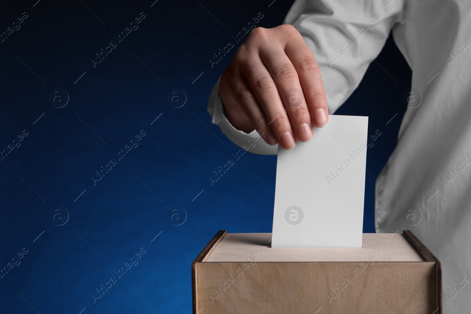 Photo of Woman putting her vote into ballot box on dark blue background, closeup. Space for text