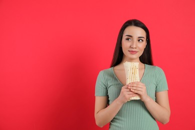 Dreamy young woman holding tasty shawarma on red background. Space for text