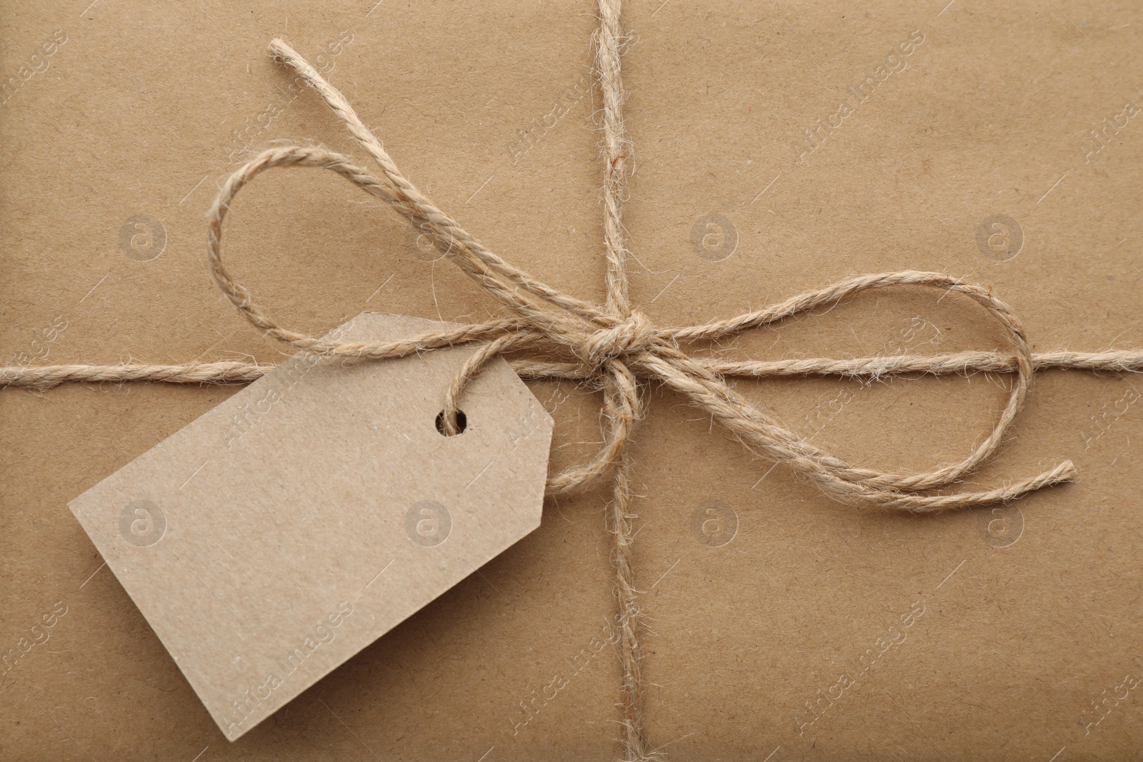 Photo of Parcel wrapped in kraft paper with tag as background, closeup