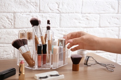 Photo of Woman taking liquid foundation from organizer for makeup cosmetic products on dressing table
