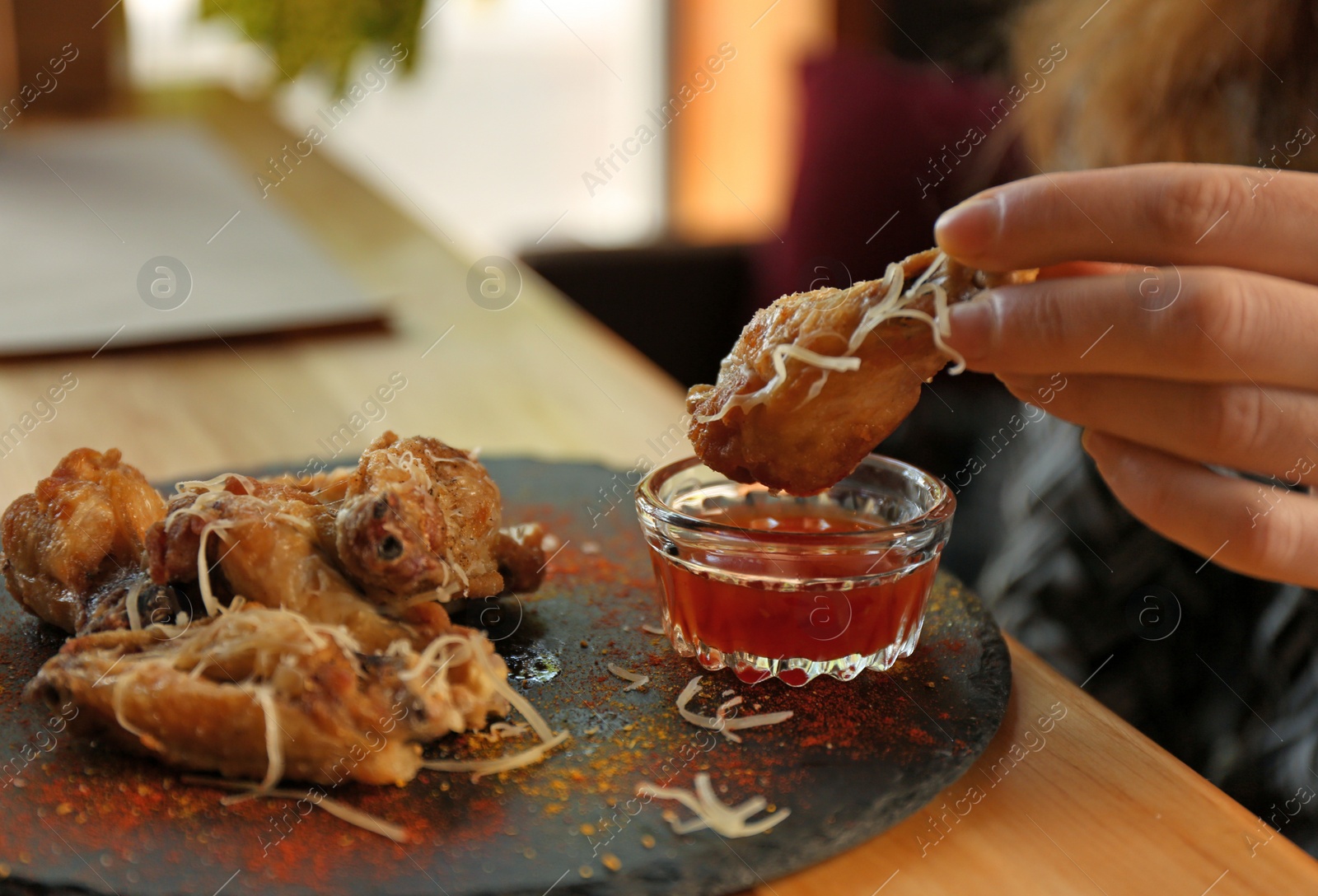 Photo of Woman dipping tasty BBQ wing into sauce at table, closeup