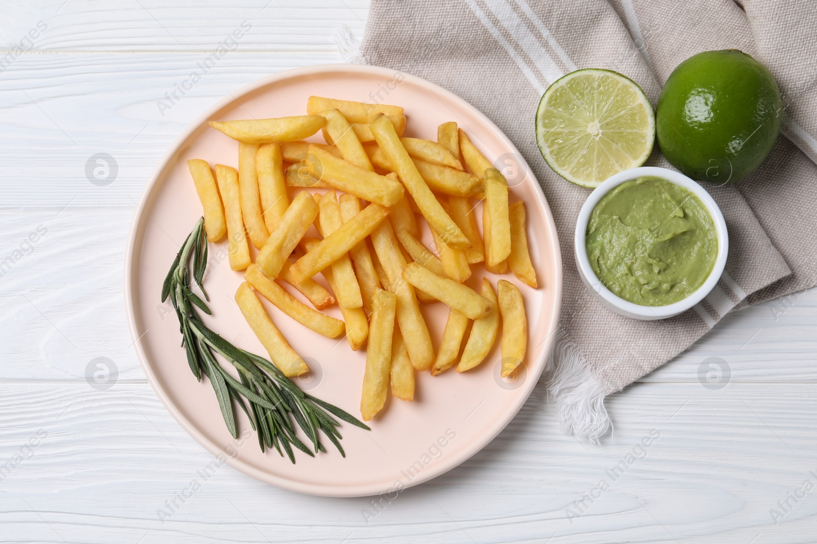 Photo of Plate with french fries, avocado dip, rosemary and lime served on white wooden table, top view