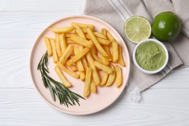 Plate with french fries, avocado dip, rosemary and lime served on white wooden table, top view