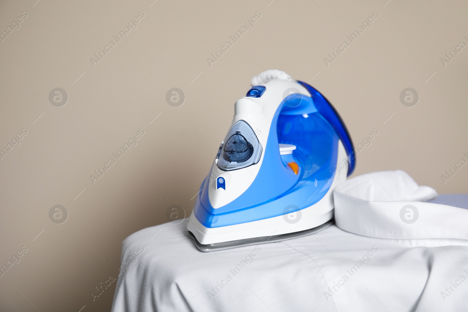 Photo of Modern iron and clean shirt on board against beige background, space for text