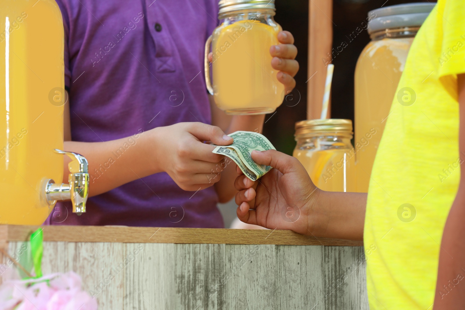 Photo of Little boy selling natural lemonade to African-American kid in park, closeup. Summer refreshing drink