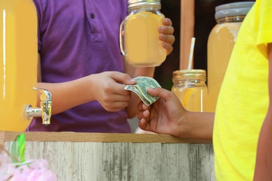 Little boy selling natural lemonade to African-American kid in park, closeup. Summer refreshing drink