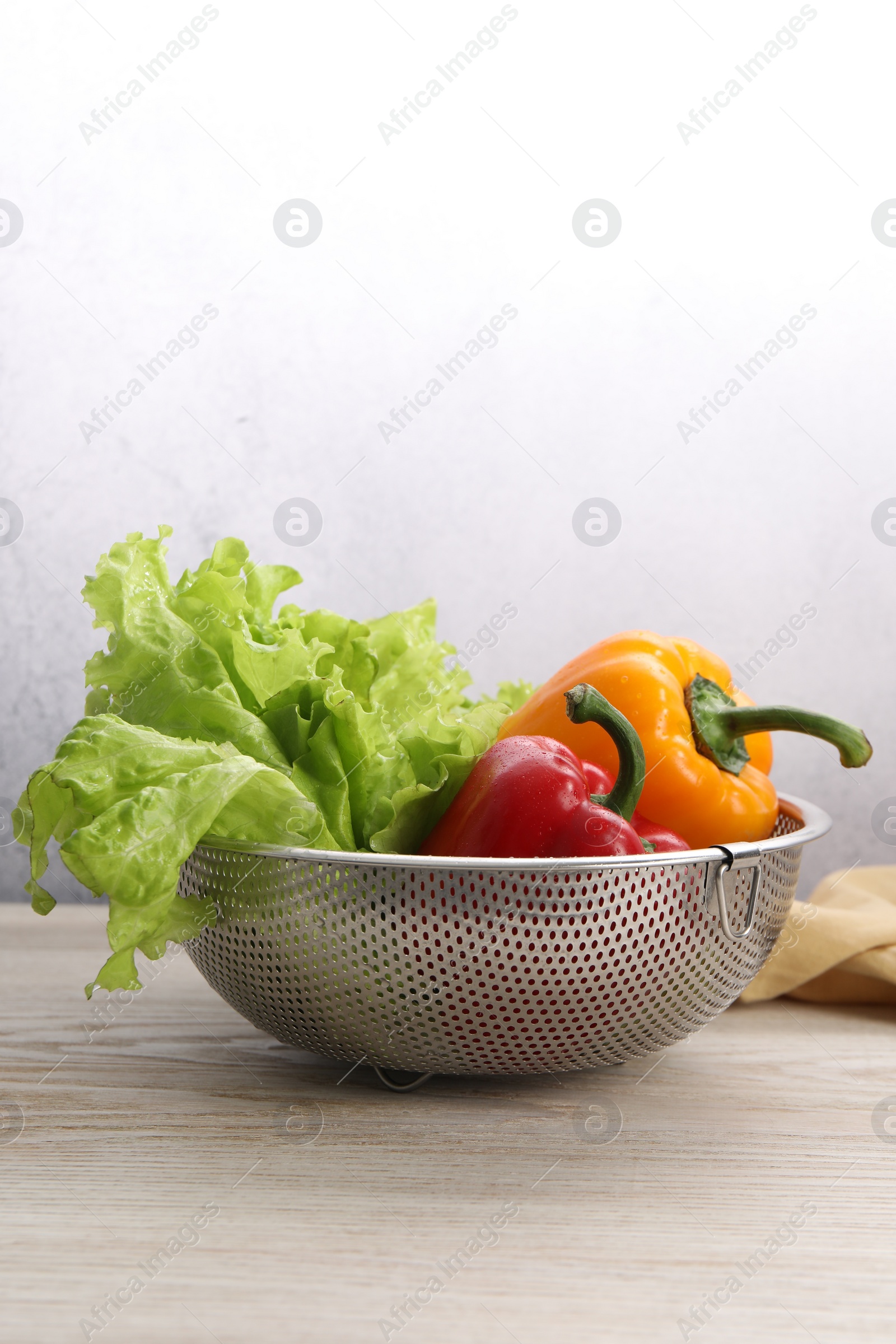 Photo of Colander with fresh lettuce and bell peppers on wooden table