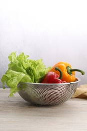 Colander with fresh lettuce and bell peppers on wooden table