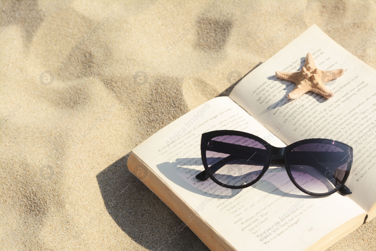 Photo of Beautiful sunglasses, book and starfish on sand. Space for text