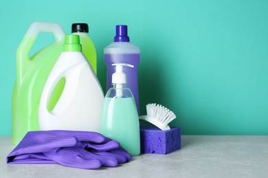 Photo of Different cleaning supplies and tools on table against turquoise background, space for text