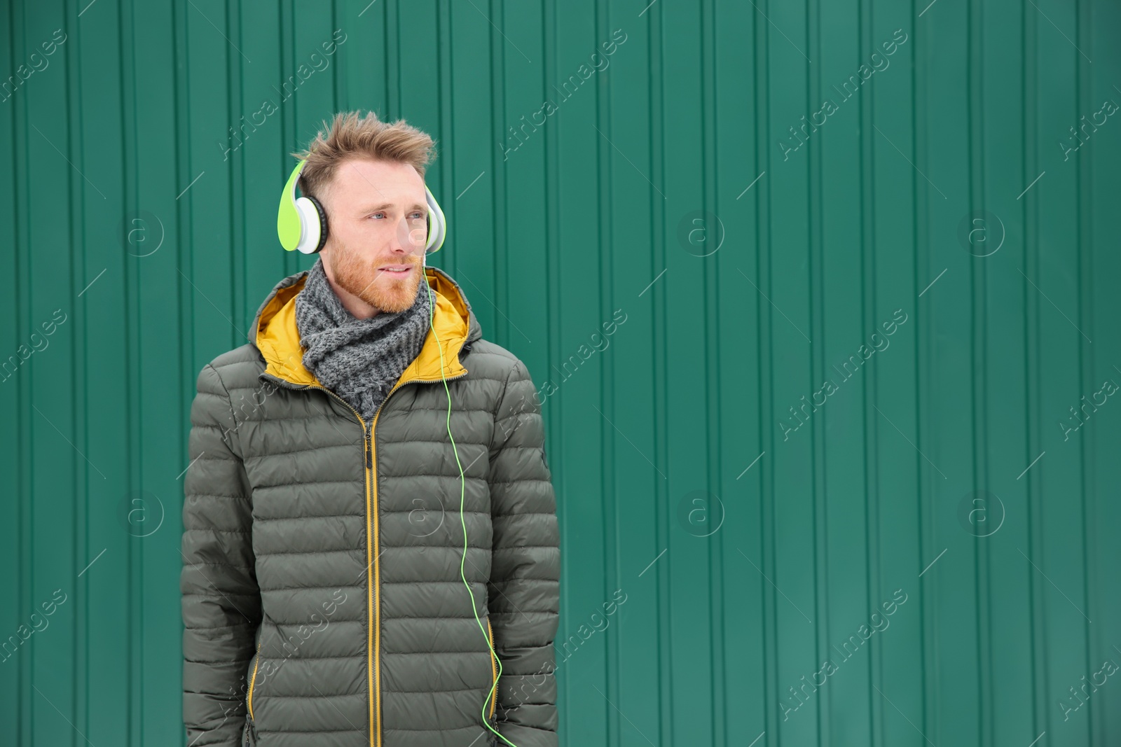 Photo of Young man listening to music with headphones against color wall. Space for text