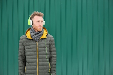 Young man listening to music with headphones against color wall. Space for text