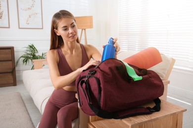 Woman packing sports stuff for training into bag at home